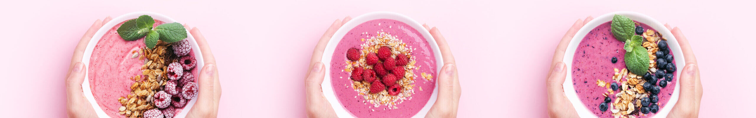 Creative image with three pair of hands holdaing smothie bowls with berries and granola on pink background. Top view, copy space, banner for website.